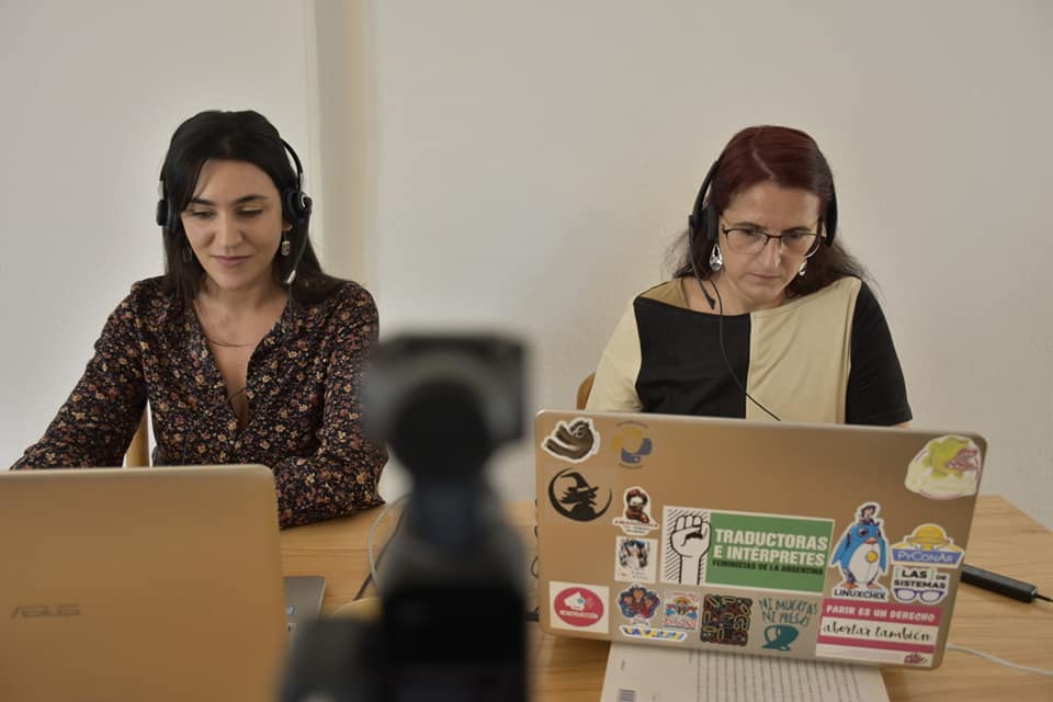 La fotografía muestra a Maitén Vargas y Erika Cosenza sentadas frente a sus respectivas laptops. Hay una cámara que las está filmando.