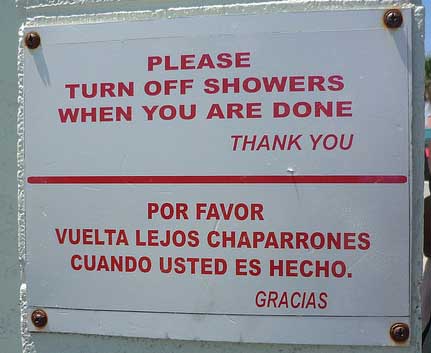 A sign reads «Turn off showers when you are done» in English and «Vuelta lejos chaparrones cuando usted es hecho» in Spanish