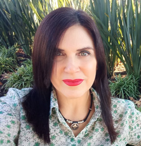 Foto de Romina Navarro. Está mirando de frente a cámara, es morocha y de ojos claros. Tiene los labios pintados de rojo y una camisa gris con arabescos verdes.