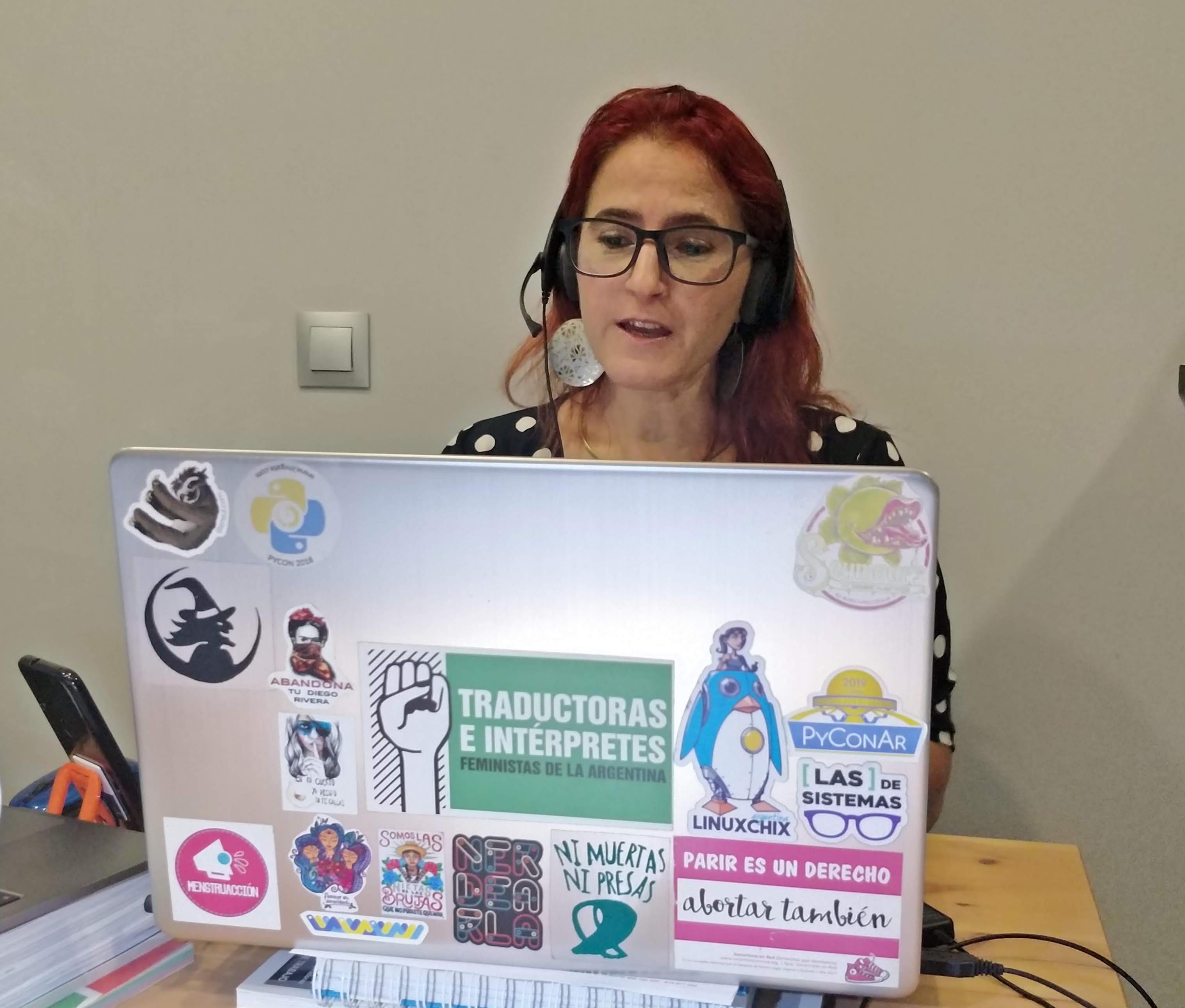 La imagen muestra a Erika Cosenza sentada frente a su laptop. Lleva auriculares con micrófonos y está hablando.